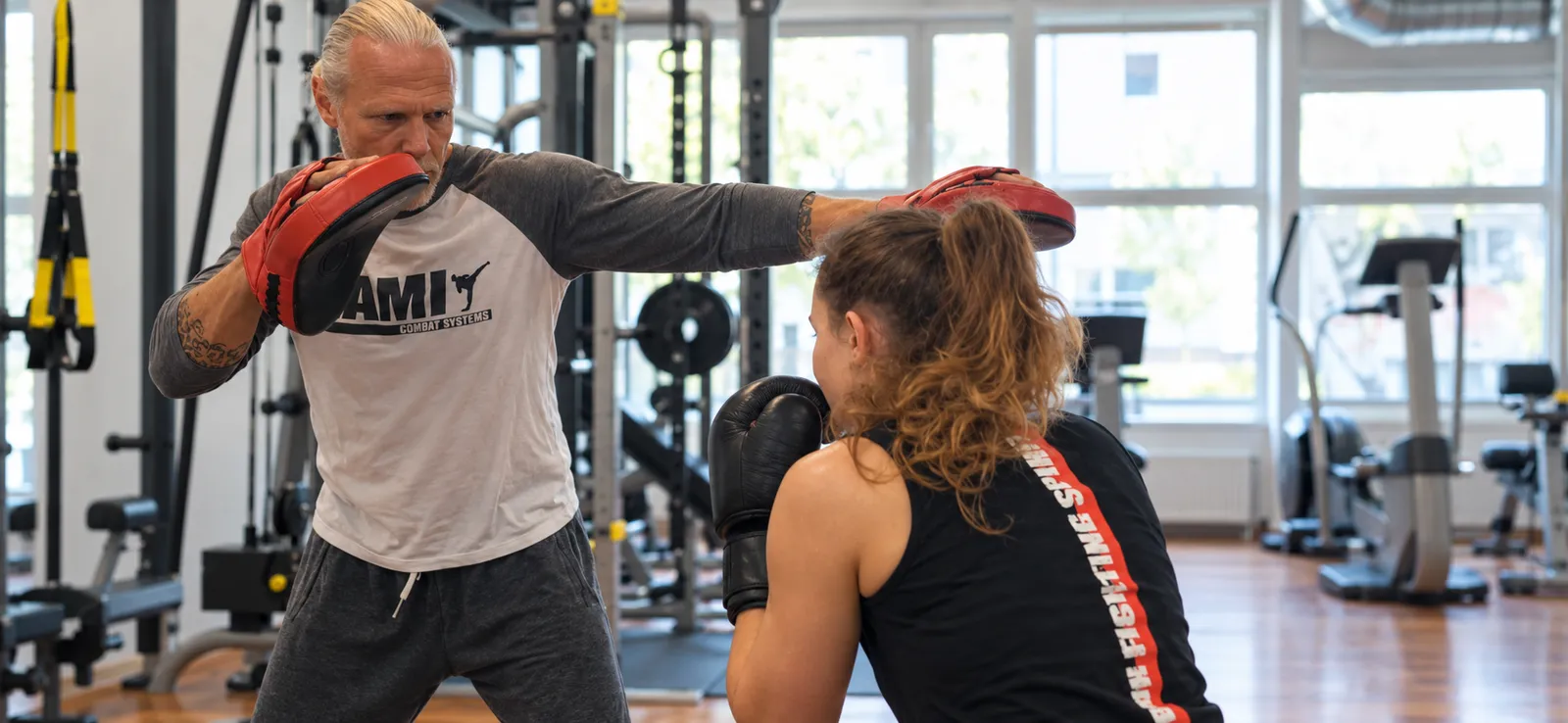 Ein Trainer zeigt einer Teilnehmerin einen geraden Schlag mit der Pratze